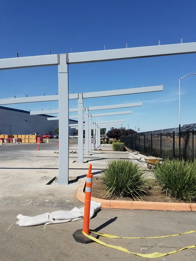 White steel columns and beams of solar shade structures along a parking lot, blue sky, traffic cone and caution tape