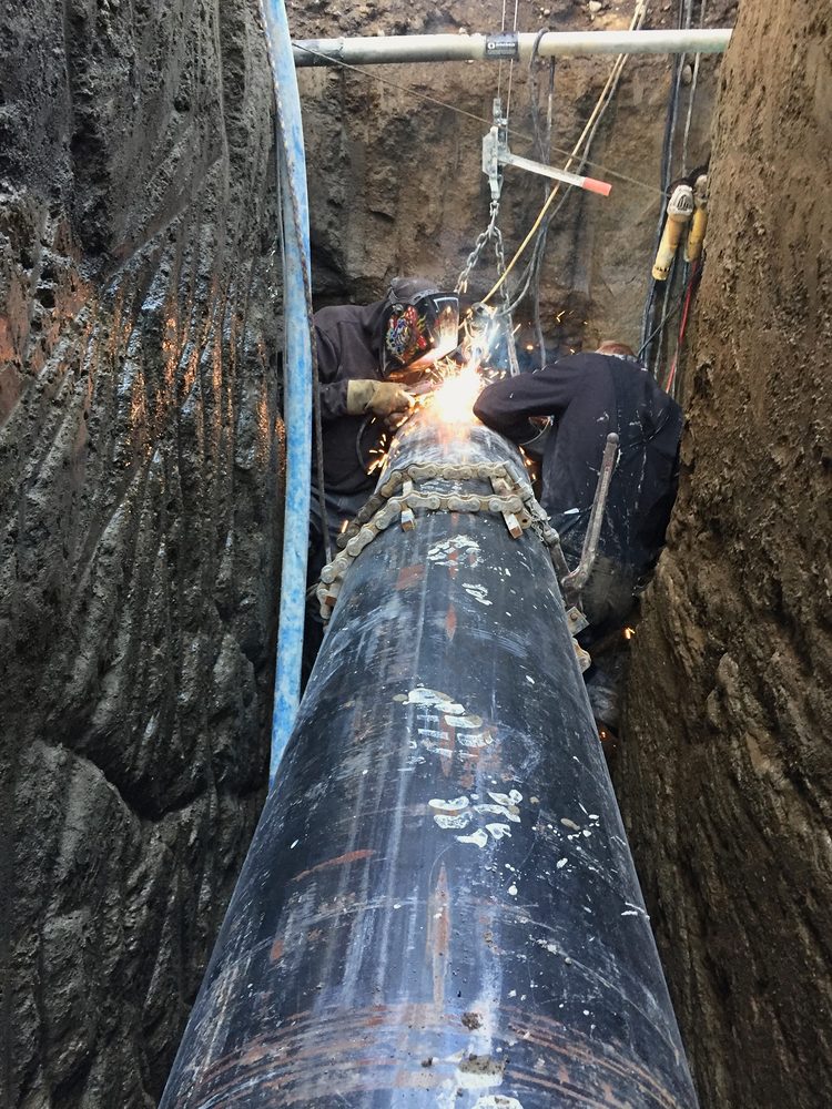 Welders joining a large steel pipe in a trench