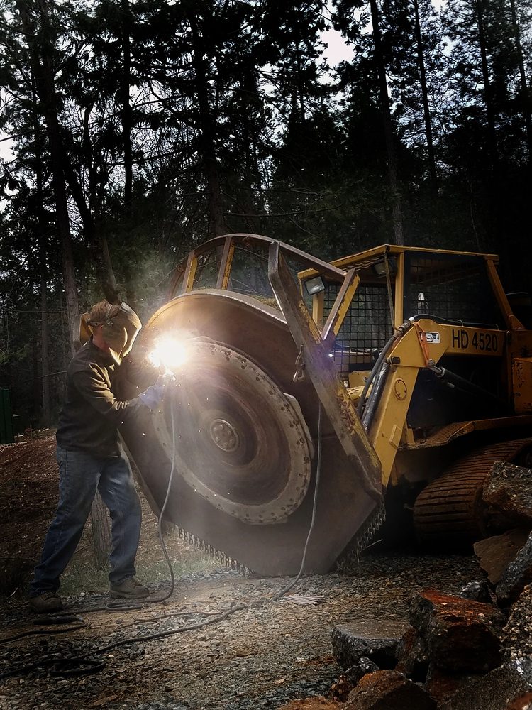 Welder repairing a mulcher drum on site in the woods