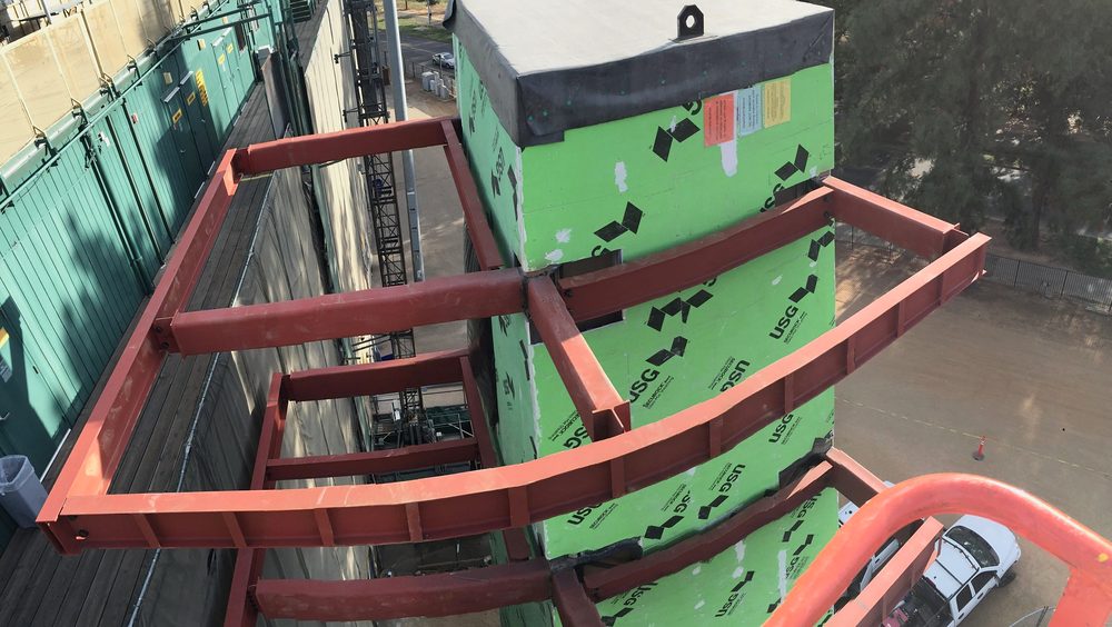 Red steel elevator outrigger frame from above, green-sheathed shaft, lift basket