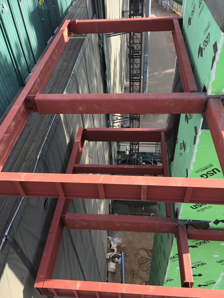 Red primed steel elevator outrigger frame from above, tight between buildings